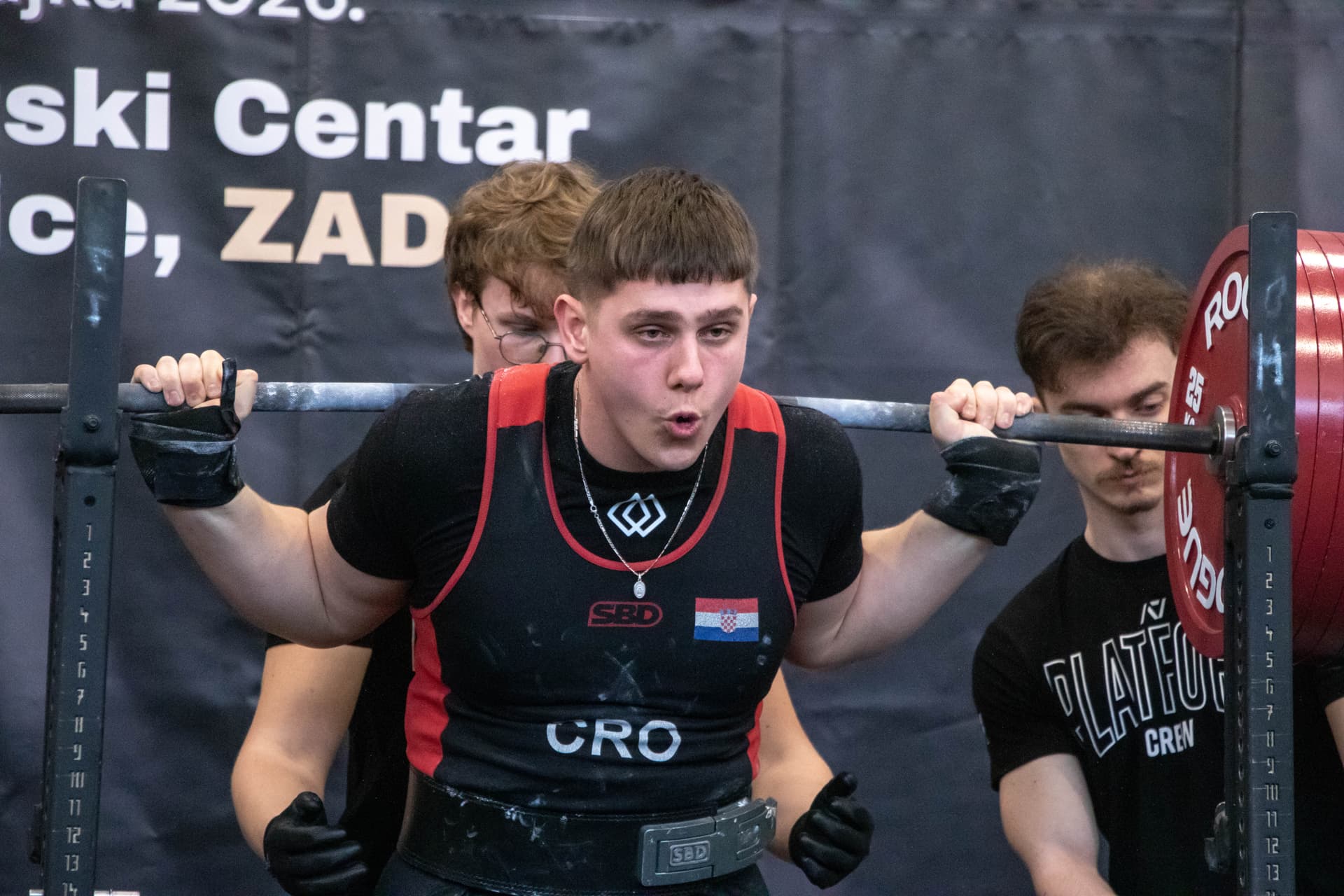 Lifter u natjecateljskom dresu s oznakom CRO, sa šipkom na leđima, priprema se za čučanj
